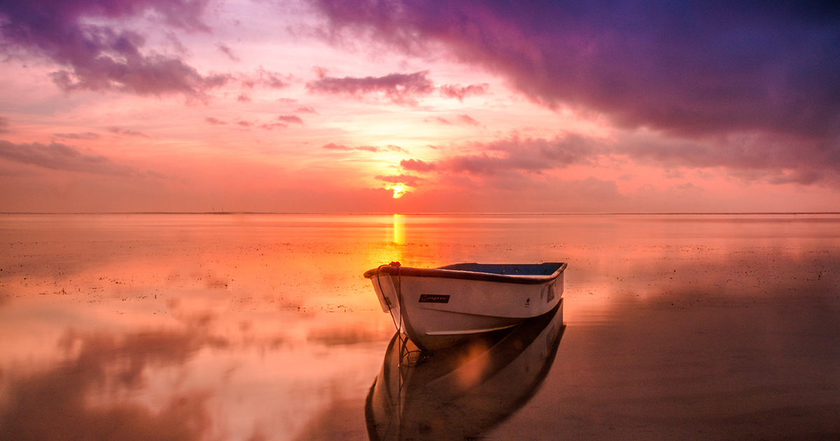 A rowboat rests on still, golden waters, as a path of melted honey leads to the rising sun on the horizon, with purple clouds making way for day.