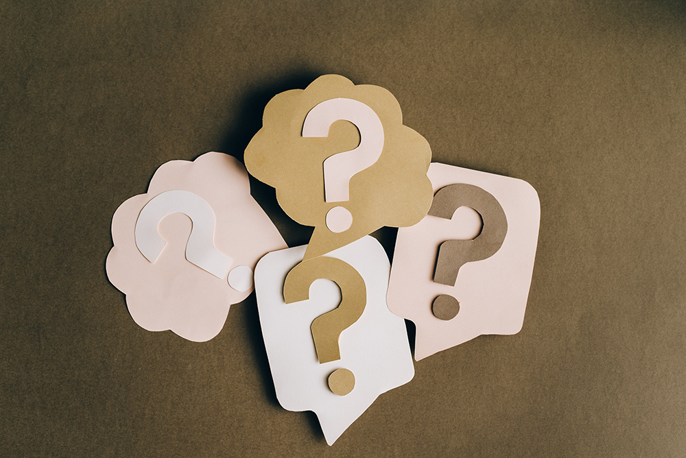 A series of question marks decoratively made from die cut paper on thought and speech bubbles.